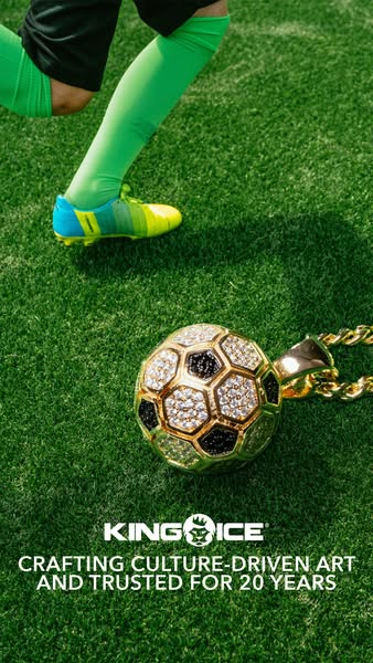 A close up of a gold and jewel encrusted soccer ball pendant from King Ice, placed on artificial turf with a soccer play