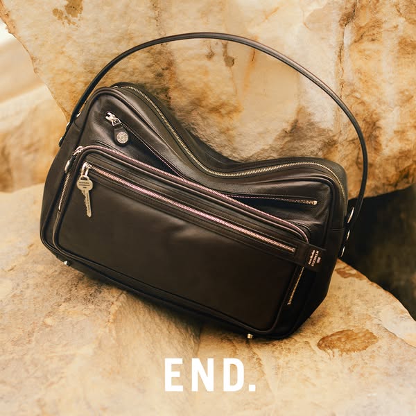 This ad showcases a black leather bag with a curved handle, positioned on a textured stone surface. The focus is on the 
