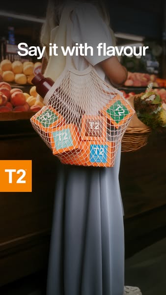 This image ad by T2 Tea shows a person carrying a mesh bag full of T2 Tea boxes at a grocery store or market. The ad'