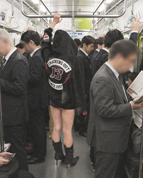 A full shot of a person wearing a hoodie with a graphic on the back and wearing boots on a subway.