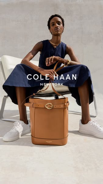 This ad showcases a model wearing a Cole Haan dress and sneakers while sitting and holding a Cole Haan handbag.