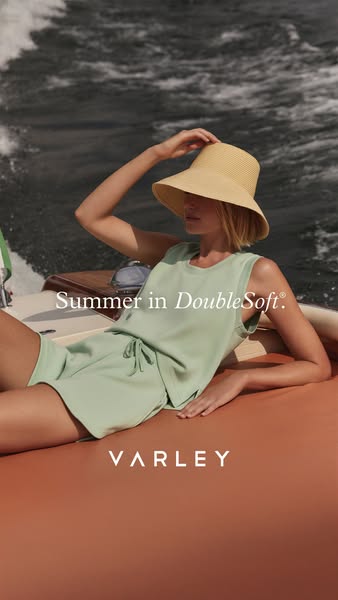 This ad showcases Varley's DoubleSoft activewear set in a lifestyle context. A person is lounging on a boat, wearing