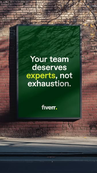 A close-up of a Fiverr billboard ad on a brick wall promoting the hiring of experts over exhausting a team.